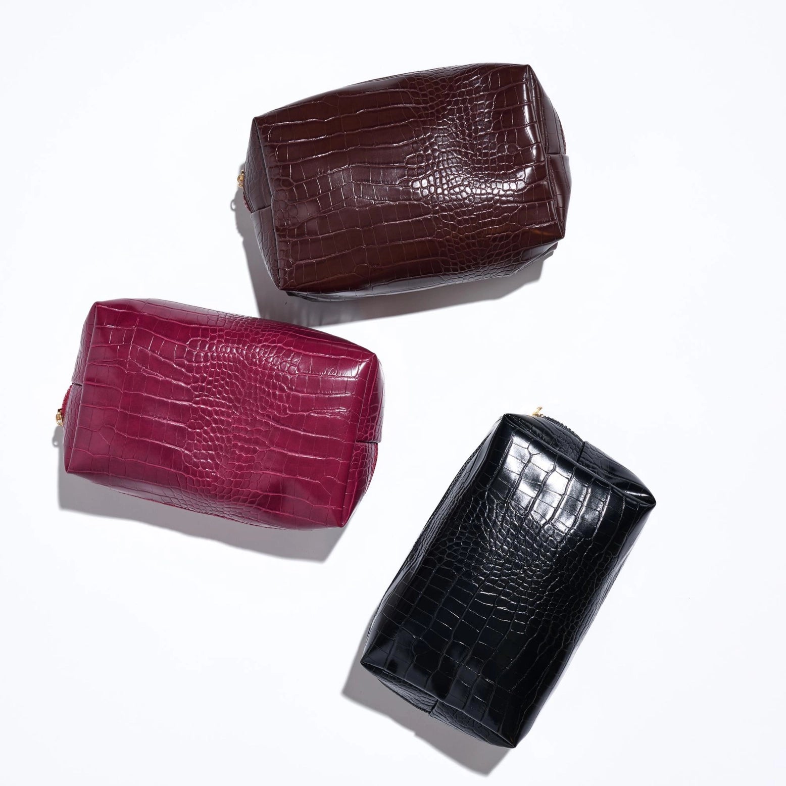 Three crocodile skin handbags in brown, red, and black on a white background